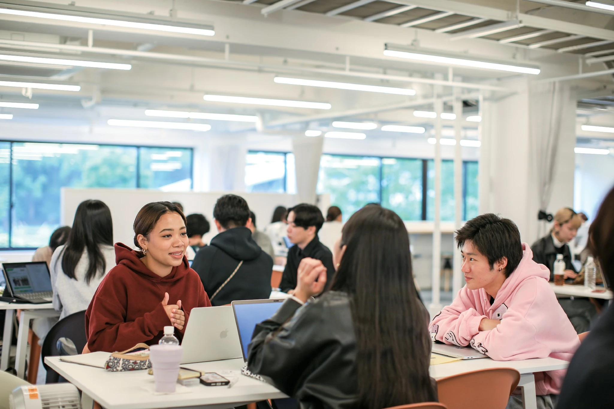 明るい教室でパソコンを開き仲間と話す学生たち