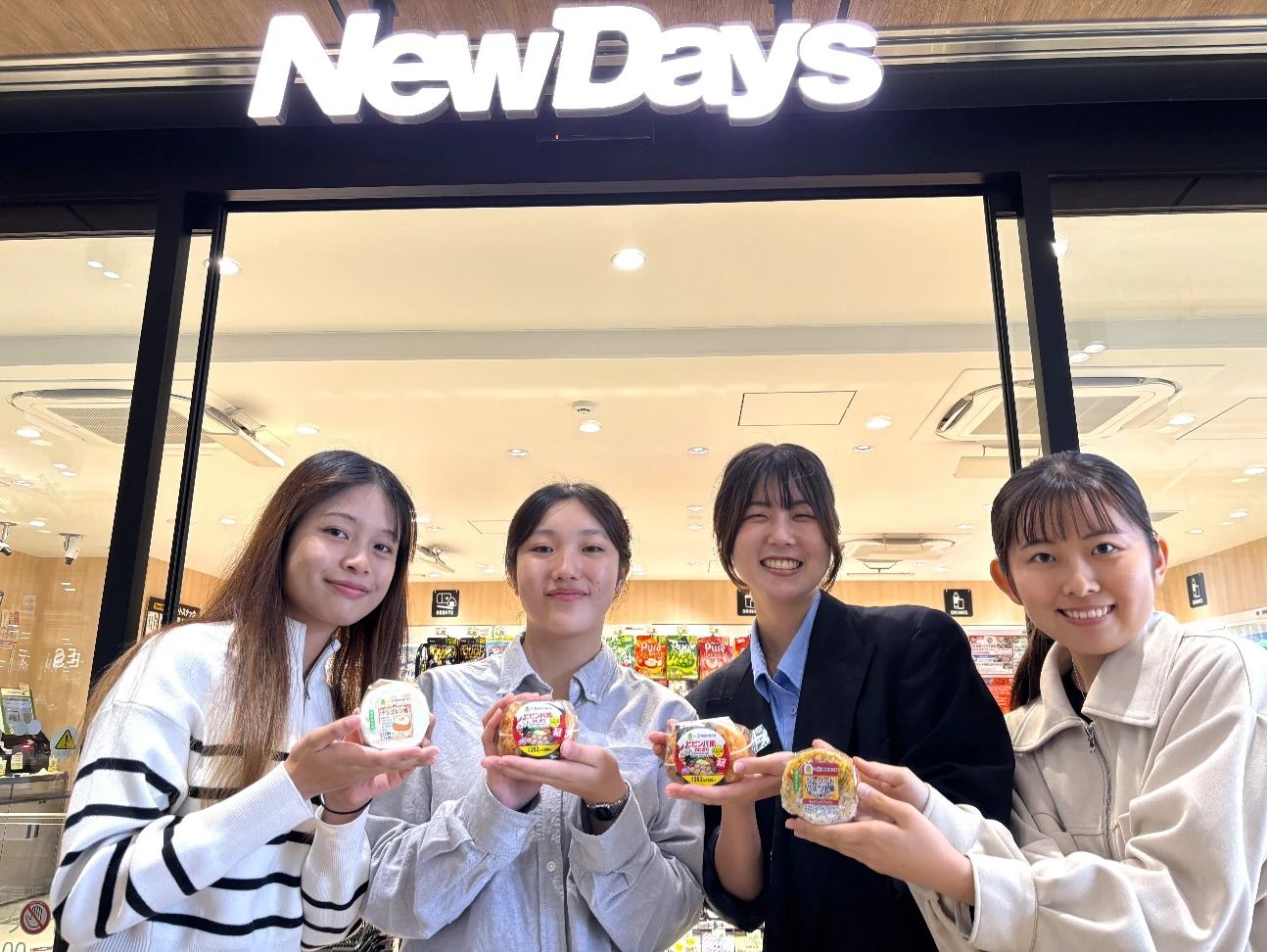 NewDaysの店舗前で共同開発した商品を持つ鶴岡ゼミの学生4人
